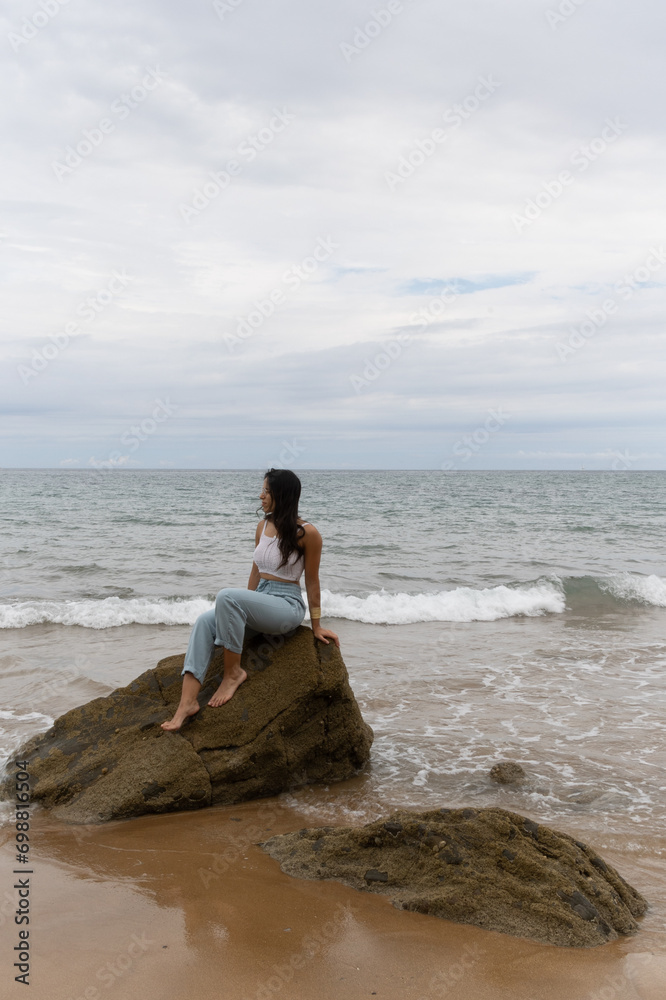Latin girl sitting on a stones in front of the sea