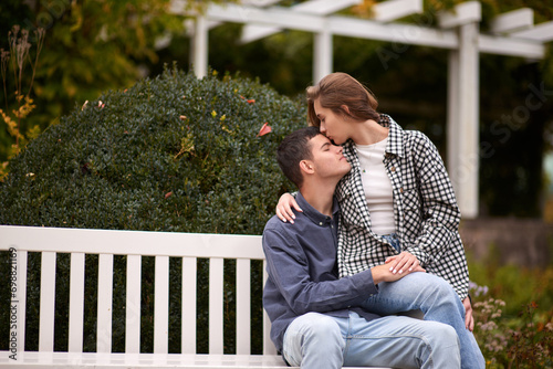 Autumn Romance: Young Couple Embracing and Kissing on Park Bench. Young couple kissing and rejoices at the lake. lovely young couple kissing outdoors in autumn. Embraced in Autumn's Warmth: Couple's © andreiko