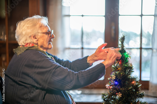 An elderly woman decorating Christmas Tree at home
