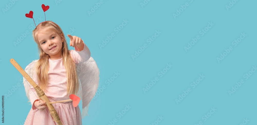 Pretty little girl dressed as Cupid with bow and arrow pointing at something on light blue background with space for text. Valentine's Day celebration Pretty little girl dressed as Cupid with bow and arrow pointing at something on light blue background with space for text. Valentine's Day celebration