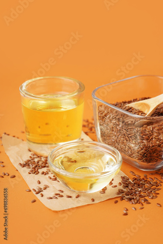 Glass with flax oil and bowl of seeds on orange background