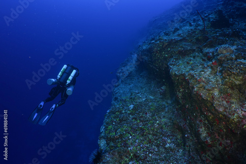 Scuba diver swim along a tropical wall near Maui, wearing a closed circuit rebreather. A rocky reef grows on the back wall at molokini crater.