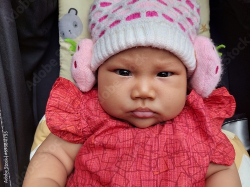 Cute Asian baby wearing a red dress and wearing a knitted hat, riding in a black stroller