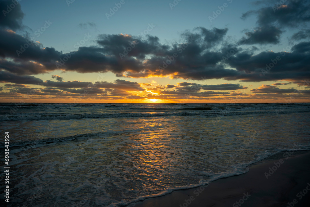 Evening landscape of sea water waves crushing on sandy beach at sunset