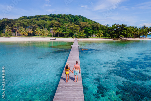 couple walking at a wooden pier in the ocean of Koh Kham Trat Thailand, aerial view of the tropical island near Koh Mak Thailand. white sandy beach with palm trees and big black boulder stones  photo