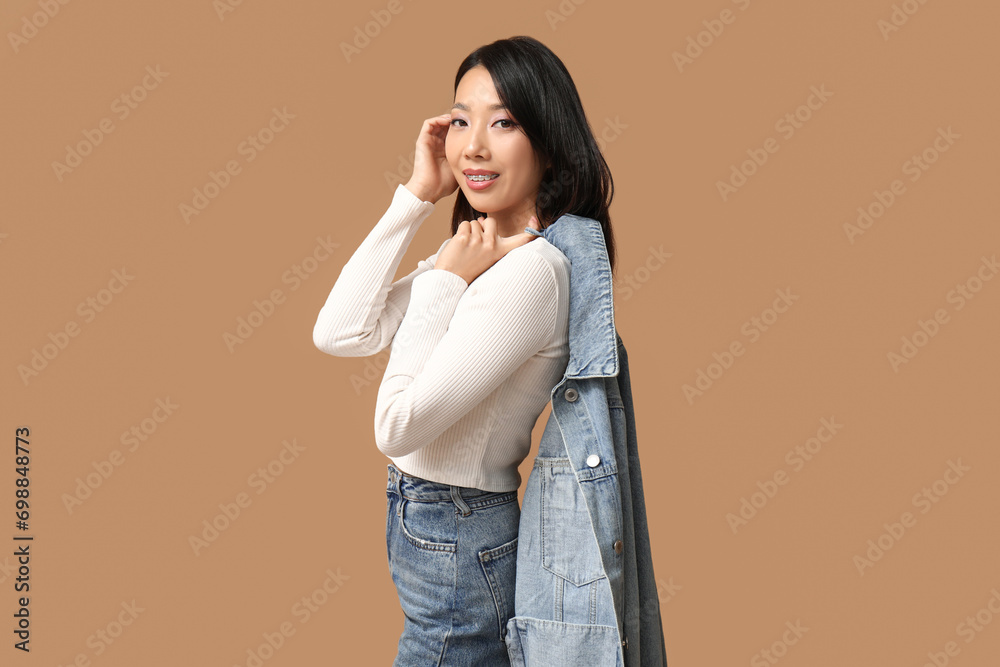 Beautiful young happy Asian woman in stylish denim clothes on brown background Beautiful young happy Asian woman in stylish denim clothes on brown background