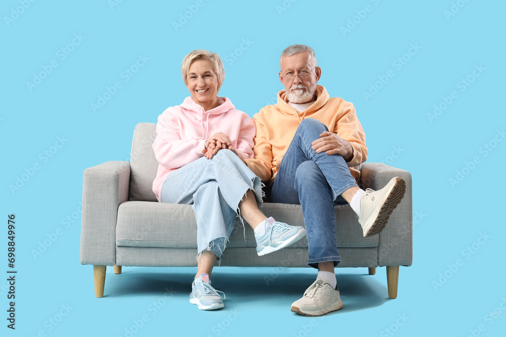 Mature couple sitting on sofa against blue background Mature couple sitting on sofa against blue background