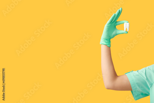 Female hand with plastic tooth on yellow background. World Dentist Day