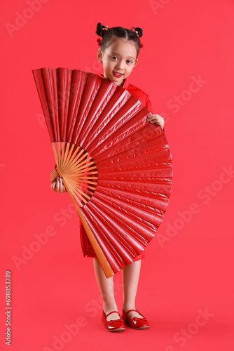 Cute little Asian girl with big fan on red background. Chinese New Year celebration