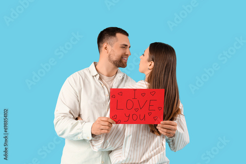 Lovely couple holding greeting card with text I LOVE YOU on blue background. Valentine's Day celebration