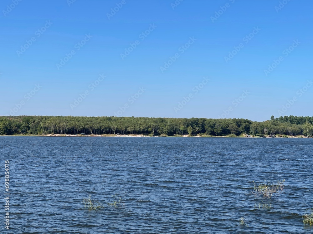 Beautiful riverscape on a windless early summer evening. The blue of the open river against the blue sky