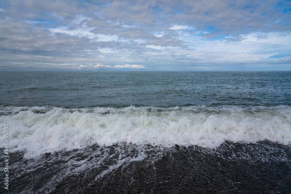 An incoming wave on the Black Sea and a pebble beach on the Sochi coast on a summer day with clouds, Sochi, Krasnodar Territory, Russia
