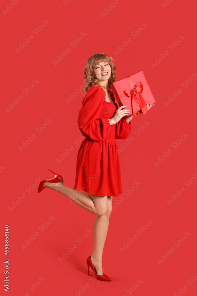 Beautiful young woman with gift box on red background. Valentine's Day celebration