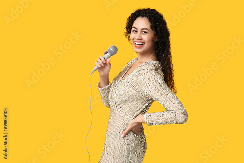 Beautiful young happy African-American female singer with microphone on yellow background