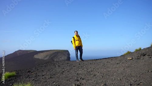 Adventurous young man visiting Vulcao dos Capelinhos and smiling on windy day, front view photo