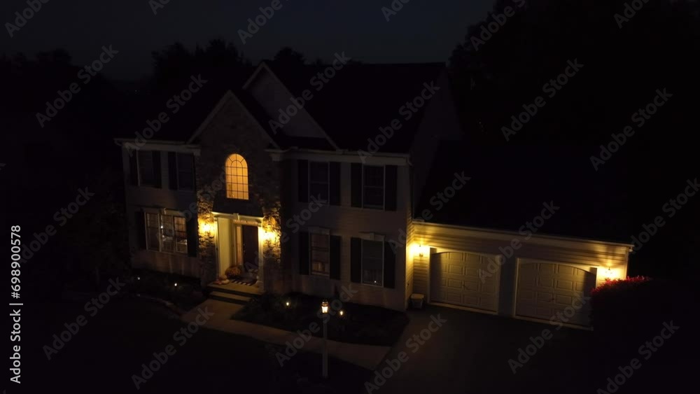 American Colonial two story home at night with garage and front porch lights on. Aerial push in shot.