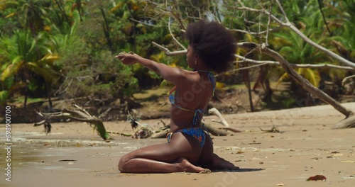 On a sunny day, a girl with curly hair in a bikini finds joy on a tropical Caribbean island beach kneel in the sand photo