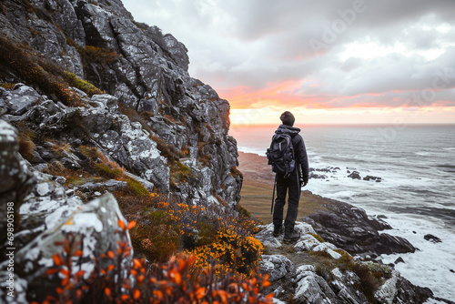 A lone traveler stands on a cliff watching a stunning sunset over a rugged coastline, evoking a sense of adventure and tranquility.