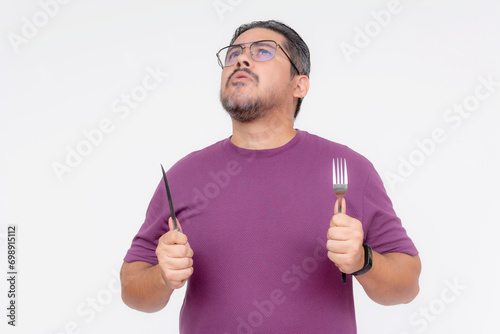 A hungry middle aged man holding a fork and knife anticipating his next meal. Yearning for and visualizing the most delicious meal. Isolated on a white background.