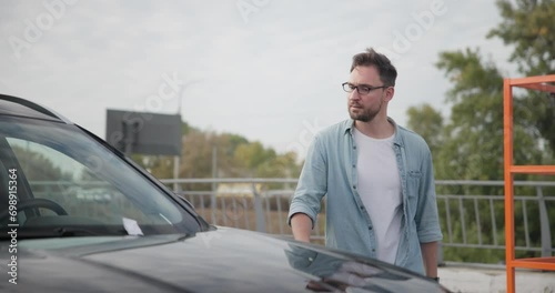 Young man comes to car and finds Parking Ticket Or Fine On Car Windshield photo