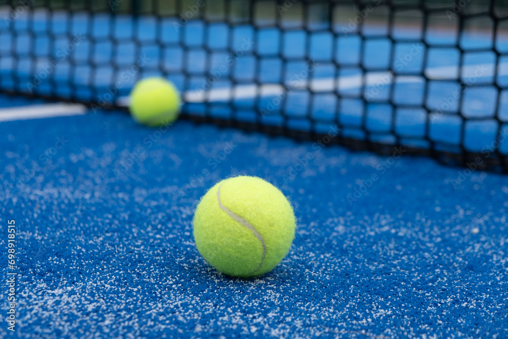 Two balls near the net of a blue padel tennis court, racket sports
