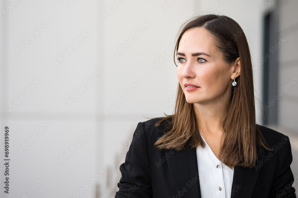 Serious adult businesswoman dressed in formal suit stands next to office confidently looking away. Lifestyle of elegant business lady concept Serious adult businesswoman dressed in formal suit stands next to office confidently looking away. Lifestyle of elegant business lady concept