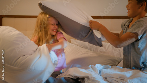 Happy funny playful Caucasian children boy girl brother sister kids siblings friends pillow fighting in bedroom on bed fooling around together playing carefree at home fight with pillows having fun