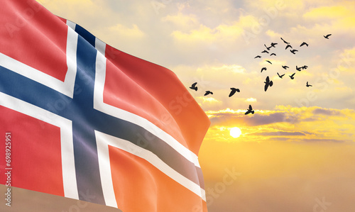 Waving flag of Norway against the background of a sunset or sunrise. Norway flag for Independence Day. The symbol of the state on wavy fabric. photo