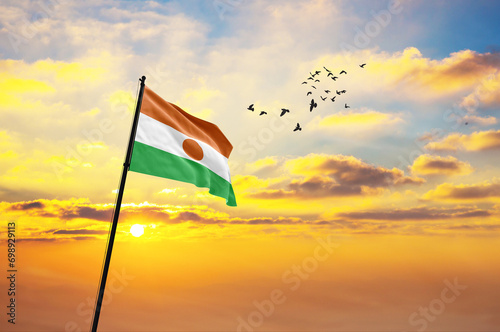 Waving flag of Niger against the background of a sunset or sunrise. Niger flag for Independence Day. The symbol of the state on wavy fabric.