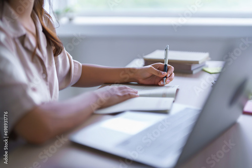 Young asian student in casual clothes watching tutorial and writing knowledge data on notebook while learning and studying lecturer education online class with laptop digital technology in university