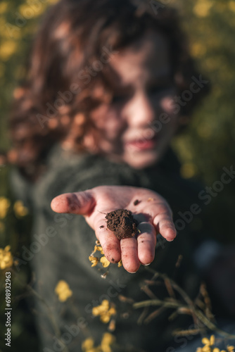 detail portrait of piece of earth in the hand of a little boy who shows it to the camera happy and content on bright sunny day on green meadow