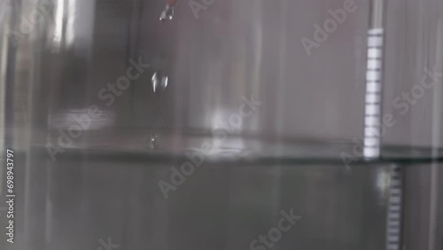 alcohol distilling process closeup - liquid distilled transparent liquid flowing in large glass jar with floating alcoholometer in it. photo