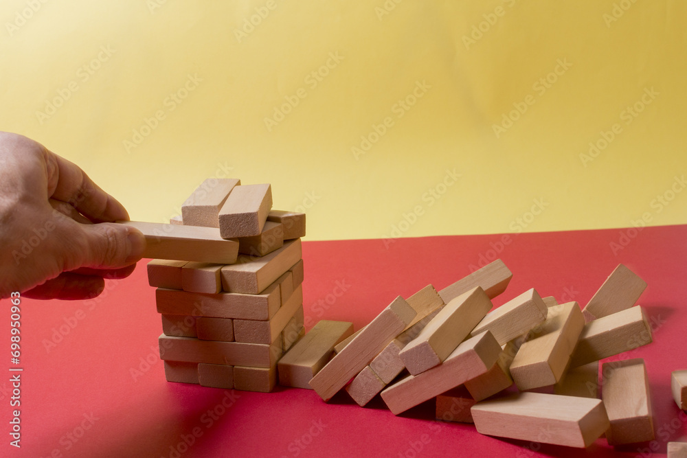 Closeup image of a hand holding and playing Jenga or Tumble tower wooden block game Closeup image of a hand holding and playing Jenga or Tumble tower wooden block game