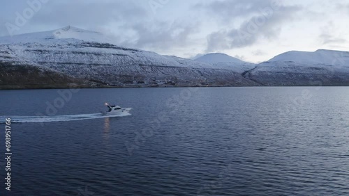 Faroe Islands, 4K Aerial tracking three quaeter shot of fishing boat with snow covered mountains in the background