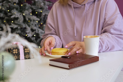 Working online during Christmas. Young cheerful blonde female in warm hoody smiling while chatting with friends using her laptop, sitting in cozy cafe. Winter holidays. Businesswoman, graphic designer