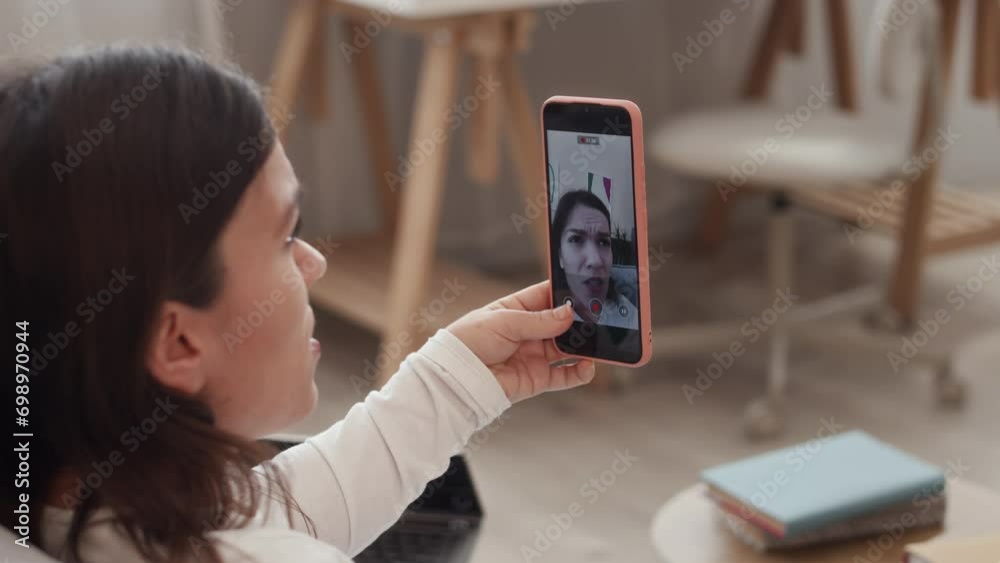 Medium closeup of young Caucasian woman with dwarfism sitting on couch in living room and recording video of herself on smartphone, sharing stories on camera Medium closeup of young Caucasian woman with dwarfism sitting on couch in living room and recording video of herself on smartphone, sharing stories on camera