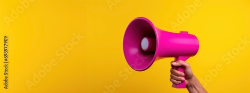Hand holding bright pink megaphone on yellow background for advertising campaign photo