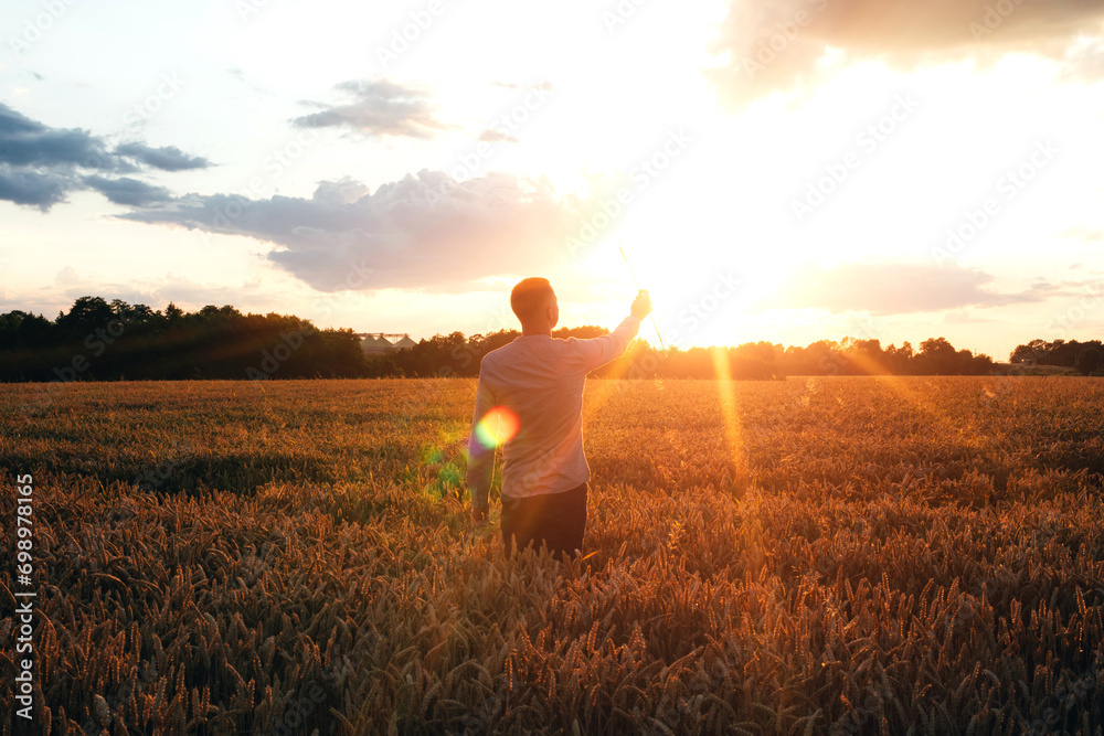 Fototapeta premium Wheat field at sunset. Agriculture concept, a farmer in the field checks the quality of the crop