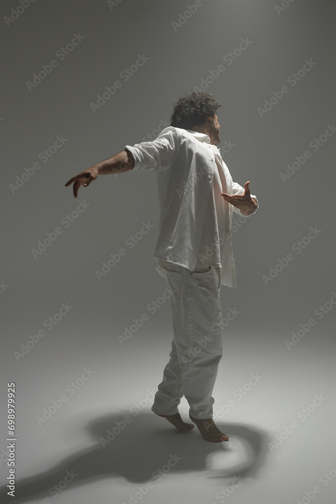 Full shot of man in white outfit dancing lightly on empty photoshoot set Full shot of man in white outfit dancing lightly on empty photoshoot set