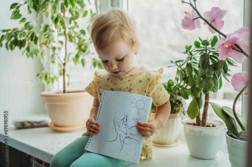 Girl sitting on window sill and showing drawing photo