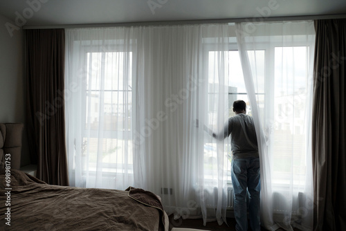 Man looking through window in bedroom at home photo