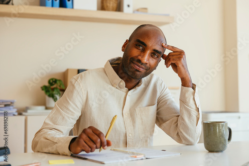 Smiling businessman leaning on elbow and writing in diary at home office desk photo