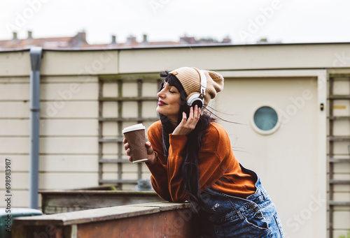Smiling woman holding coffee cup and enjoying music through wireless headphones photo