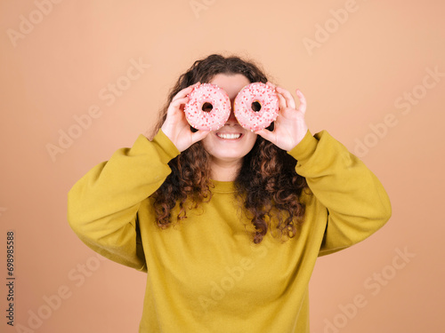 Playful woman holding doughnuts over eyes against peach background photo