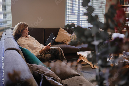 Mature woman sitting on sofa and using tablet PC at home photo