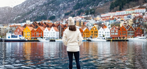 A tourist woman enjoys the panoramic view of the colorful Bryggen district in Bergen, Norway, during a cold winter day