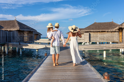 A beautiful family walks over a wooden pier between water lodges in the Maldives islands during their vacations