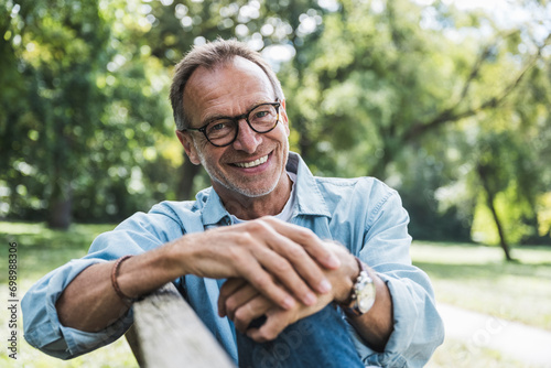 Smiling senior man with eyeglasses sitting on bench in park photo