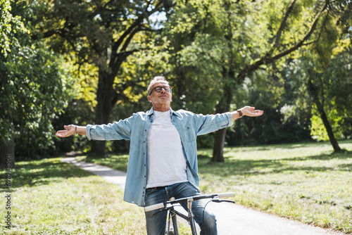 Carefree senior man with arms outstretched sitting on bicycle in park photo