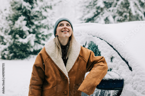 Woman wearing winter coat and leaning on car in snow photo